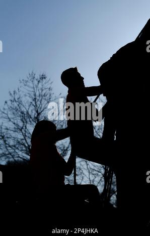 Atleti che si arrampicano su un ostacolo utilizzando una corda in una corsa OCR. Foto Stock