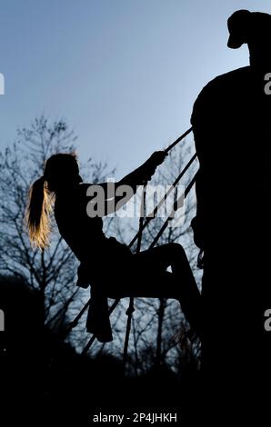 Atleta femminile che si arrampica su un muro in una corsa a ostacoli Foto Stock