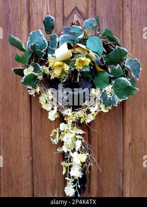 Una corona stagionale fatta di edera e fiori gialli su una porta in pannelli di legno. Foto Stock