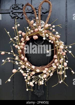 Una corona stagionale fatta di bacche rosa e bianche su una porta rivestita di pannelli scuri. Foto Stock