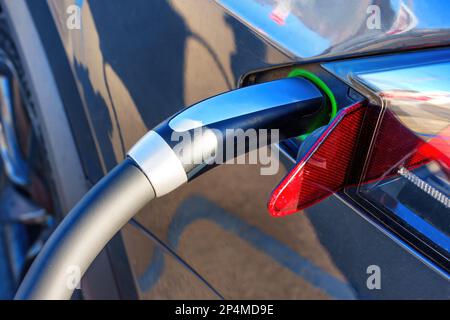 L'auto elettrica viene caricata con una vista ravvicinata del connettore collegato al veicolo. Foto Stock