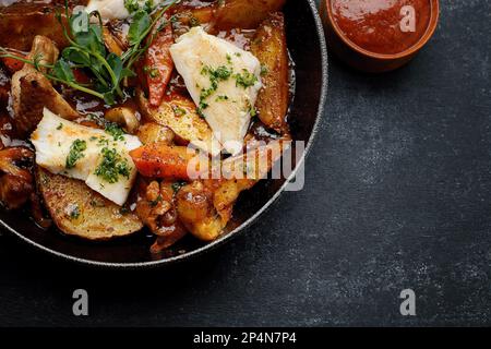 Patate fritte in salsa, con funghi, verdure, pollo e formaggio, in una padella Foto Stock