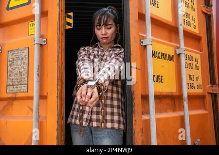 Donna intrappolata nel contenitore di carico attendere il traffico di esseri umani o lavoratori di fronte, donna che tiene la chiave padronale in attesa di aiuto holp, donna incatenata al suo wrinis Foto Stock