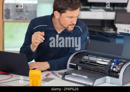 L'uomo sporgendoti fotocopiatore aperto durante le riparazioni di manutenzione Foto Stock