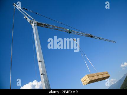 Gru da cantiere con carico appeso di asse in legno su un cielo blu Foto Stock