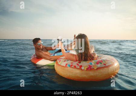 Coppia con bicchieri di vino e anelli gonfiabili in mare Foto Stock