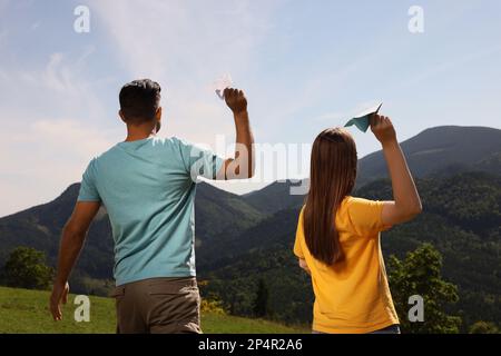 Coppia che lancia aerei di carta in montagna il giorno di sole, vista posteriore Foto Stock