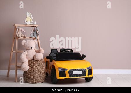 Auto elettrica per bambini con altri giocattoli vicino alla parete beige al coperto. Spazio per il testo Foto Stock