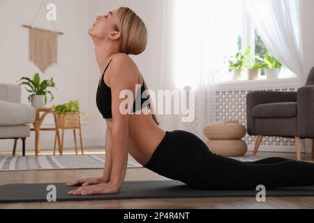 Bella donna che pratica yoga in stanza luminosa a casa Foto Stock