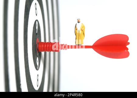 Fotografia di figura giocattolo delle persone in miniatura. Un sultano che indossa una bihst gialla (mantello di re) che si erge sopra una freccia rossa che atterrava nel centro della freccetta Foto Stock