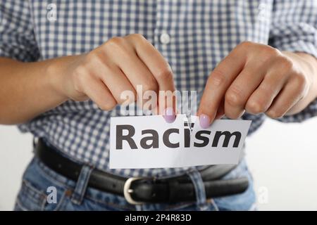 Donna strappare su foglio di carta con parola Racism su sfondo bianco, primo piano Foto Stock