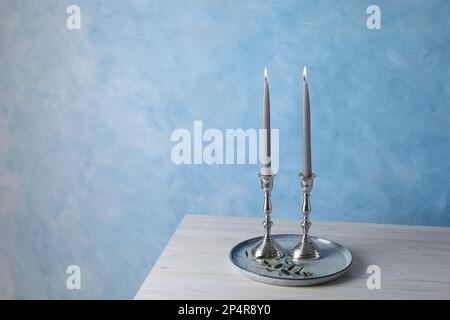 Supporti con candele bruciate su tavolo di legno vicino a parete blu chiaro, spazio per il testo Foto Stock