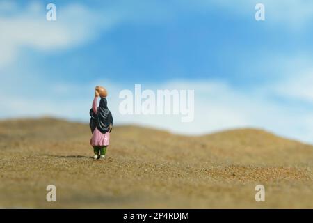 Fotografia di figura giocattolo delle persone in miniatura. Problema e problema della siccità. Le donne che indossano il velo camminano nel mezzo del dessert portando una brocca sopra la testa. Foto Stock