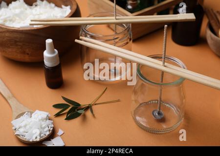 Vasetti di vetro con stoppini, scaglie di cera e olio essenziale su fondo marrone. Fare candele fatte in casa Foto Stock