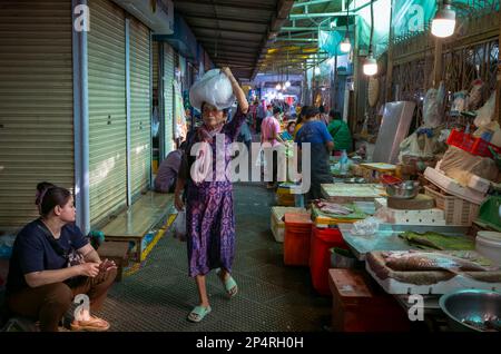 Una donna di mezza età trasporta un pacchetto sulla sua testa mentre cammina giù attraverso la sezione di pesce e frutti di mare del mercato centrale, Phnom Penh, Cambogia. Foto Stock