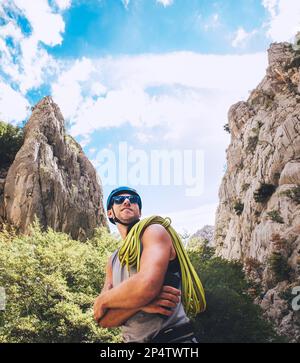 Ritratto di sorridente arrampicatore in casco protettivo e occhiali da sole con corda da arrampicata sulla spalla in piedi nel parco Paklenica tra roccia w rupe Foto Stock