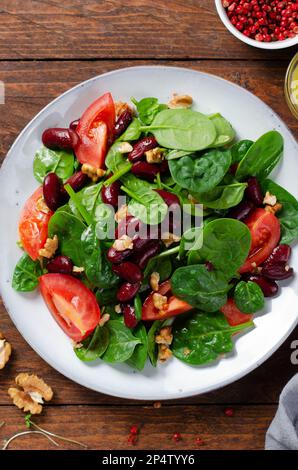 Insalata di fagioli rossi, insalata di Vegan con spinaci, pomodori ciliegini, noci, fagioli e condimento di senape su sfondo di legno Foto Stock