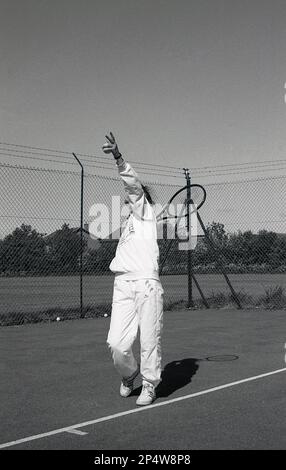 1980s, storica, fuori, su un campo da tennis hardcore, una giovane donna, in tuta, che serve una palla da tennis, Inghilterra, Regno Unito. Foto Stock