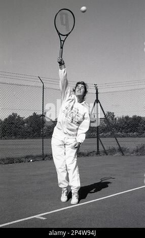 1980s, storica, fuori, su un campo da tennis hardcore, una giovane donna, in tuta, che serve una palla da tennis, Inghilterra, Regno Unito. Foto Stock