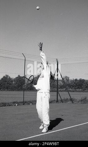 1980s, storica, fuori, su un campo da tennis hardcore, una giovane donna, in tuta, che serve una palla da tennis, Inghilterra, Regno Unito. Foto Stock