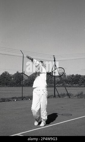 1980s, storico, fuori, su un campo da tennis hardcore, una giovane donna, in tuta, servizio, Inghilterra, REGNO UNITO. Foto Stock