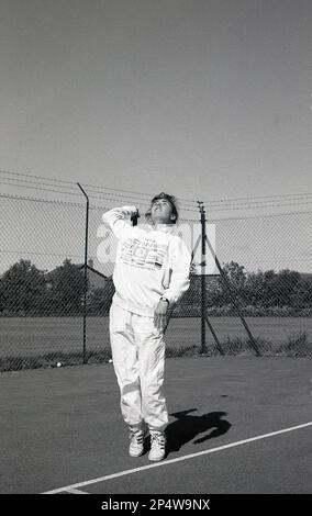 1980s, storico, fuori, su un campo da tennis hardcore, una giovane donna, in tuta, servizio, Inghilterra, REGNO UNITO. Foto Stock