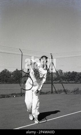 1980s, storico, fuori, su un campo da tennis hardcore, una giovane donna, in tuta, servizio, Inghilterra, REGNO UNITO. Foto Stock