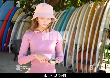 Ritratto donna surfista applica zinco protettivo sul viso. Preparazione alla navigazione. Migliore protezione da sole attivo e UV per lungo tempo. Produzione ecocompatibile Foto Stock
