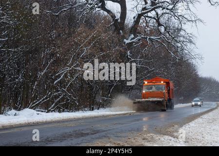 Un'auto di grandi dimensioni con un aratro libera la strada dalla neve. L'equipaggiamento speciale per il carico arancione è in difficoltà con gli elementi in inverno. Rimozione degli effetti di t Foto Stock