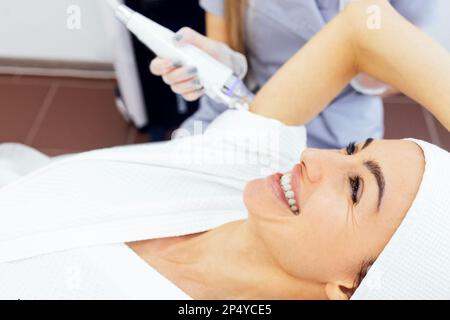 Cura della pelle del corpo. Donna caucasica sorridente che fa la rimozione dei capelli del laser delle ascelle e delle braccia. La rimozione dei capelli in metallo è fatta da bella giovane femmina. Hairles Foto Stock