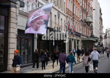 Un ritratto della defunto Regina Elisabetta II è visto come i lutto si riuniscono per rendere i loro rispetti nel centro di Londra, il giorno del suo funerale. Foto Stock