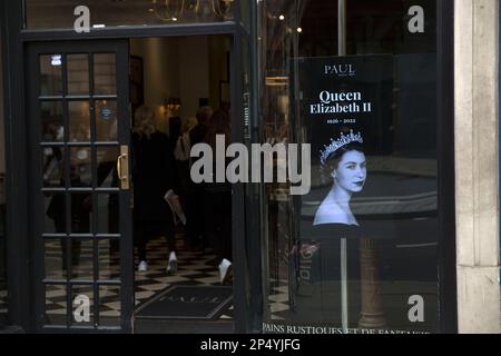 Un ritratto della defunto Regina Elisabetta II è visto come i lutto si riuniscono per rendere i loro rispetti nel centro di Londra, il giorno del suo funerale. Foto Stock