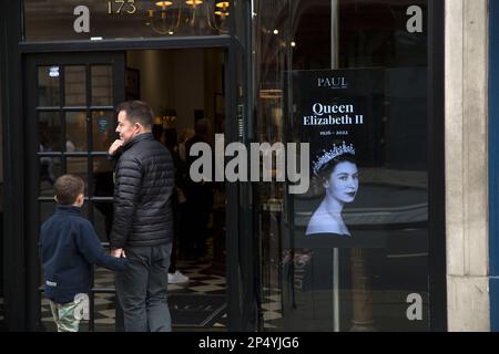 Un ritratto della defunto Regina Elisabetta II è visto come i lutto si riuniscono per rendere i loro rispetti nel centro di Londra, il giorno del suo funerale. Foto Stock