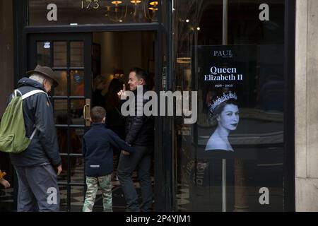 Un ritratto della defunto Regina Elisabetta II è visto come i lutto si riuniscono per rendere i loro rispetti nel centro di Londra, il giorno del suo funerale. Foto Stock