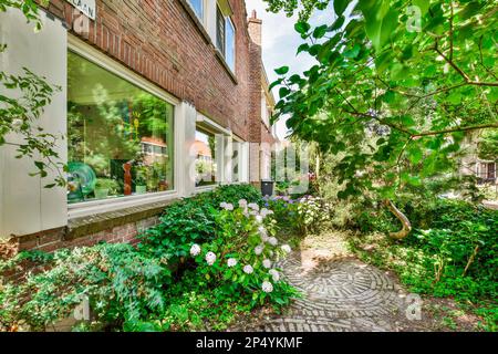 un'area esterna con piante e fiori in fronte - angolo a finestre di un edificio in mattoni, circondato da verde fogliame Foto Stock
