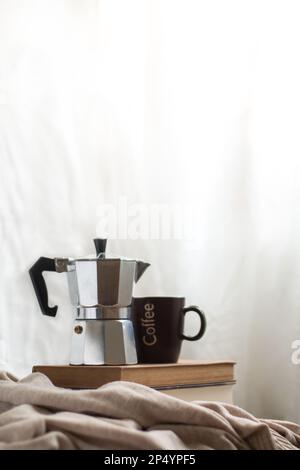 Una tazza di caffè e una moka pot su alcuni libri in uno spazio accogliente. Godersi la vita al chiuso. Foto Stock