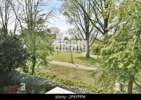un giardino con erba verde e cespugli sullo sfondo, vi è una panca circolare in pietra circondata da una vegetazione lussureggiante Foto Stock