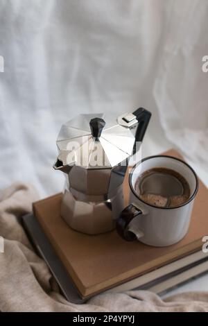 Una tazza di caffè e una moka pot su alcuni libri in uno spazio accogliente. Prospettiva superiore. Godersi la vita al chiuso. Foto Stock