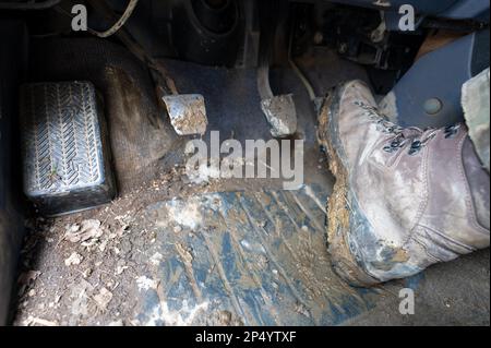 Primo piano delle gambe di un uomo in mimetizzazione militare con scarponi da trekking sporchi di fango nell'auto. Foto Stock