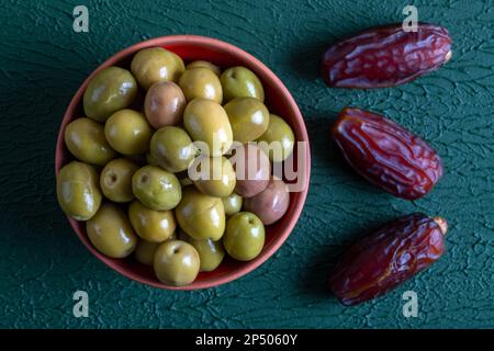 Un mazzo di frutta da datazione con una ciotola di olive verdi, su fondo verde Foto Stock