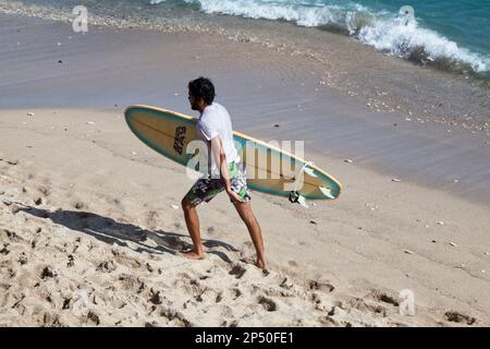 Saint-Gilles les Bains, la Réunion - Giugno 13 2017: Giovane uomo che tiene la sua tavola da surf mentre cammina ai margini della Plage des Roches Noires (Spiaggia di Foto Stock