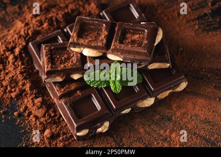 Cioccolato fondente e al latte con noci su fondo scuro cosparso di polvere di cacao. Pezzi di cioccolato con mandorle e nocciole primo piano. Foto Stock