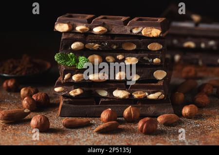 Cioccolato fondente e al latte con noci su fondo scuro cosparso di polvere di cacao. Pezzi di cioccolato con mandorle e nocciole primo piano. Foto Stock