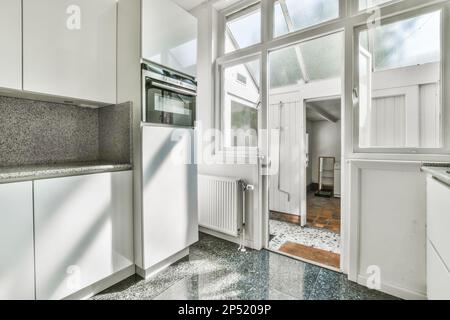 una cucina vuota con ripiani in granito e armadi bianchi su entrambi i lati, guardando fuori al sole che splende attraverso la finestra Foto Stock