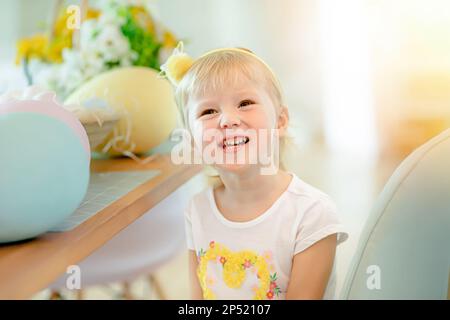 Una bambina in cucina a un tavolo da enormi uova di Pasqua. Bambini alla caccia all'uovo di Pasqua Foto Stock