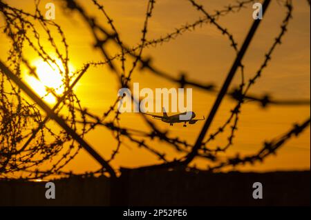 Vista attraverso il filo spinato su un aereo volante al tramonto. Foto Stock