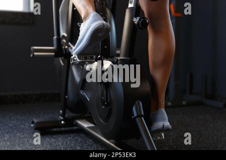 Piedi di giovane atleta allenarsi sulla macchina ellittica in palestra. Donna atletica in bicicletta al coperto su moderne attrezzature di orbitrek Foto Stock