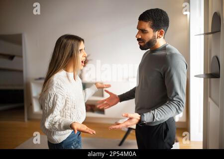 Una triste donna millenaria europea arrabbiata urla contro il tipo arabo, litigi e giuramento nel salotto interno Foto Stock