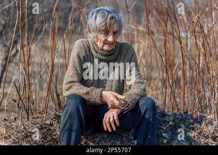 Nonna siede con uno sguardo pensivo su un mucchio di vecchio fogliame nel giardino Foto Stock