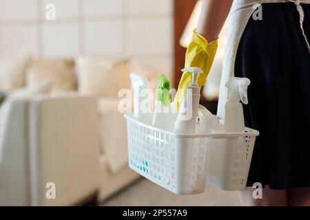 Primo piano della governante in guanti di gomma che trasportano un cestino con bottiglie di plastica contenenti detergenti mentre entra in camera d'albergo Foto Stock